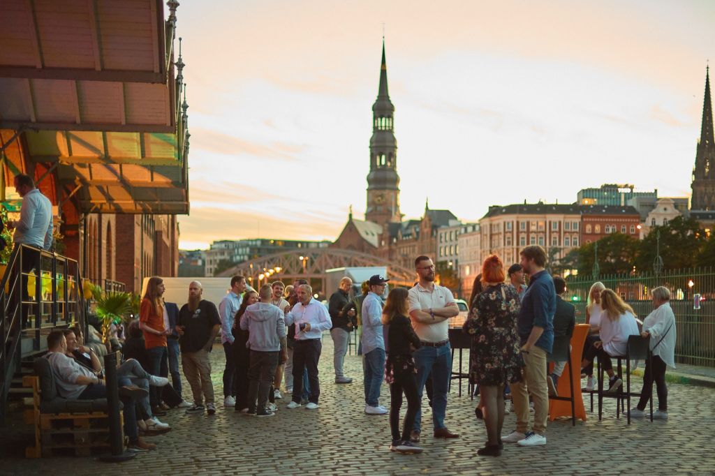 Auf dem Bild zu sehen: Gäste der 20 Jahre webgo in Sundowner Stimmung in der Hamburger Speicherstadt draußen. Im Hintergrund die wunderschöne Speicherstadt.