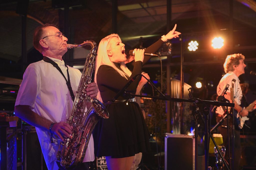 Auf dem Bild zu sehen: Voller Einsatz auf der Firmenfeier! Saxophonist und Sängerin geben alles! Im Hintergrund der Gitarrist.