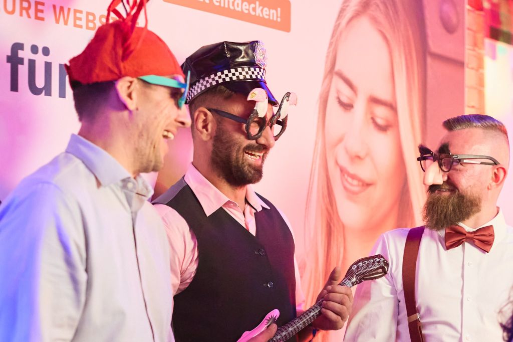 Auf dem Foto zu sehen: webgo Teammitglieder verkleidet für ein Foto vor der Fotobox. Im Hintergrund der webgo Messestand.