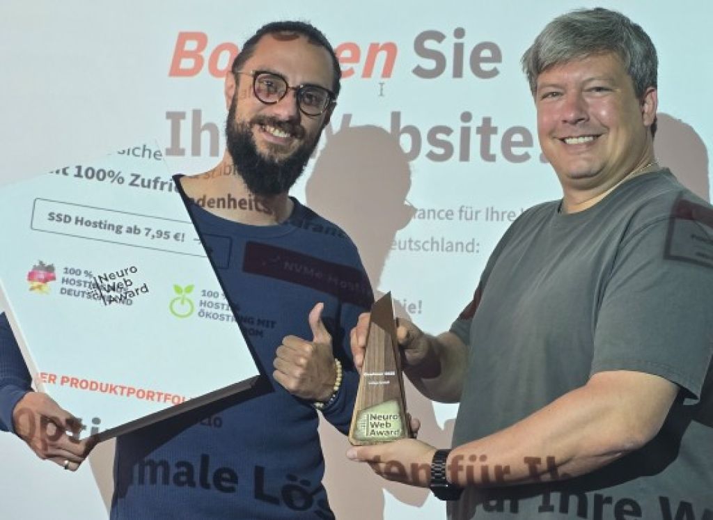 Zwei Männer (Head of Marketing Marcel El-Ghori und CTO Jan Behrens) stehen nebeneinander vor einer Wand. Ein Beamer strahlt die Webseite auf sie. Der Mann links trägt ein dunkelblaues Langarmshirt und hält eine weiße Tafel mit dem Schriftzug 'Neuro Web Award'. Der Mann rechts trägt ein graues T-Shirt und hält die Neuro Web Award-Auszeichnung als Skulptur mit der Aufschrift 'Neuro Web Award'.