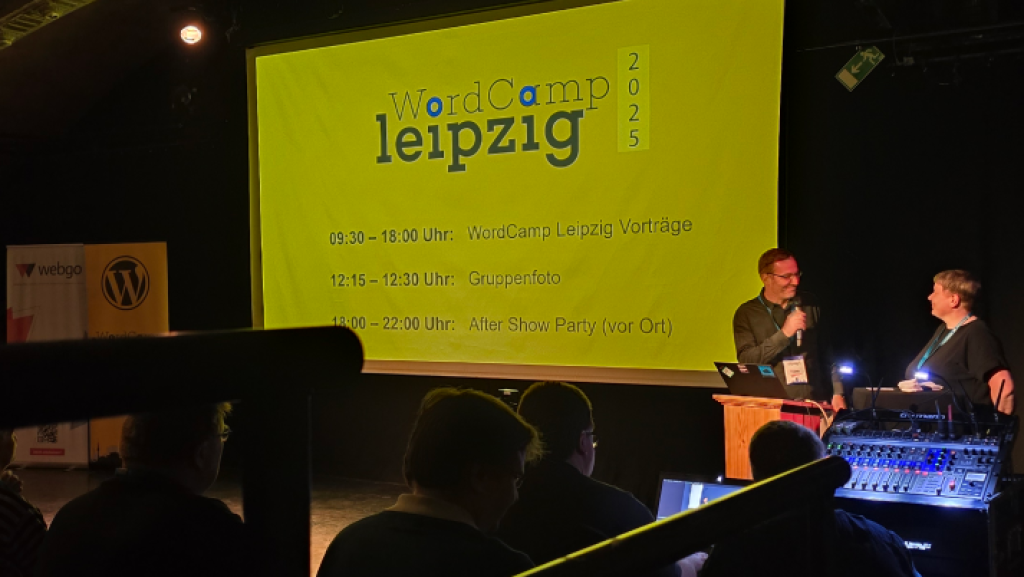 Thomas Kujawa und Jana Schlegel vom Orga-Team stehen auf der Bühne des WordCamp Leipzig 2025 vor einer Leinwand mit dem Tagesprogramm, inklusive Vorträgen und After Show Party.
