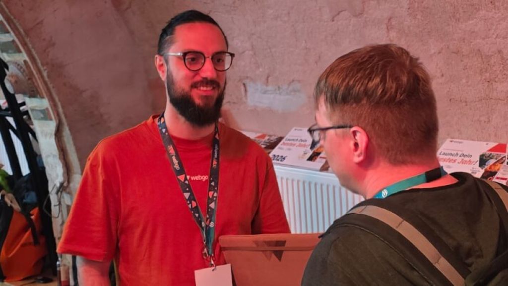 webgo's Head of Marketing Marcel El-Ghori unterh&auml;lt sich beim WordCamp Leipzig 2026 in einem Veranstaltungsraum mit einem Teilnehmer.