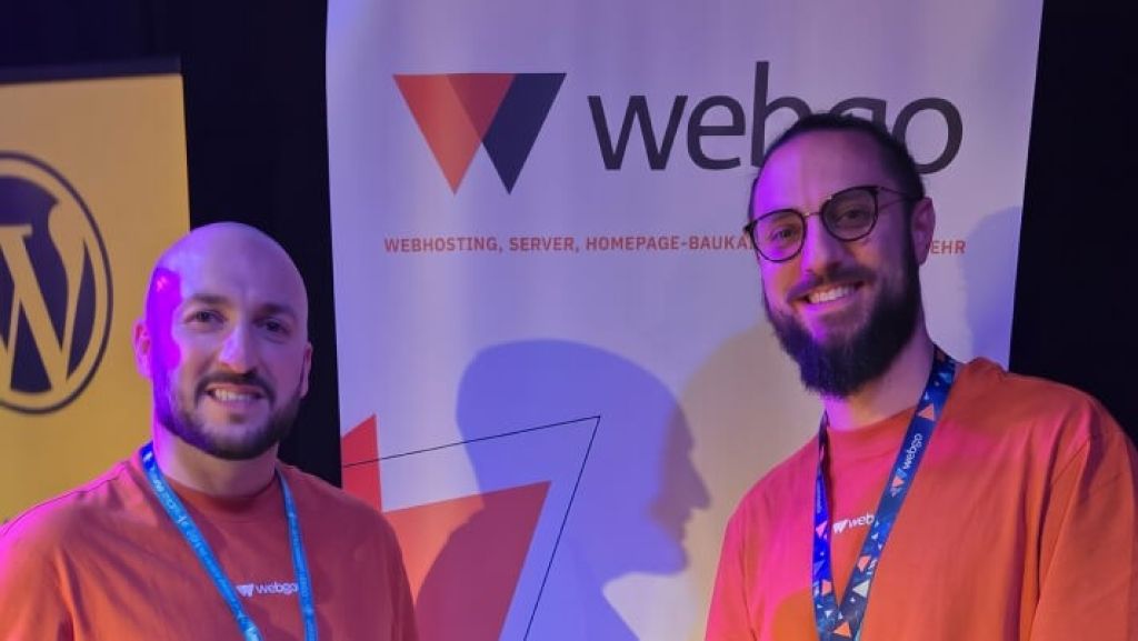 Online Marketing Manager Serhat K&ouml;yl&uuml;ce und Head of Marketing Marcel El-Ghori vor einem Roll-Up Banner mit dem webgo Logo.