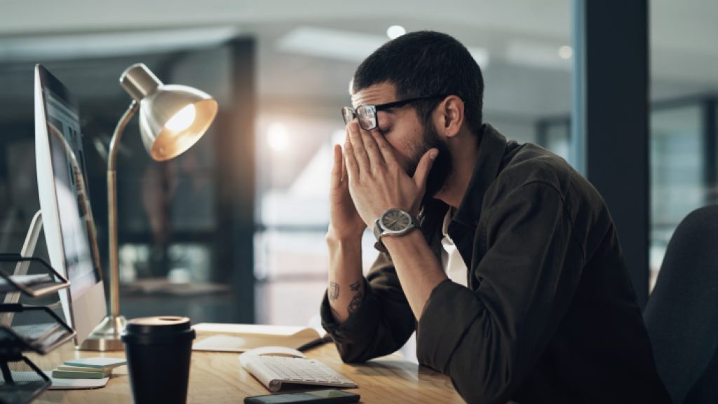 Gestresster Mann mit Brille sitzt vor dem Computer und hält sich frustriert das Gesicht – symbolisiert Ärger über kostenpflichtige E-Mail-Adressen bei Hosting-Anbietern.
